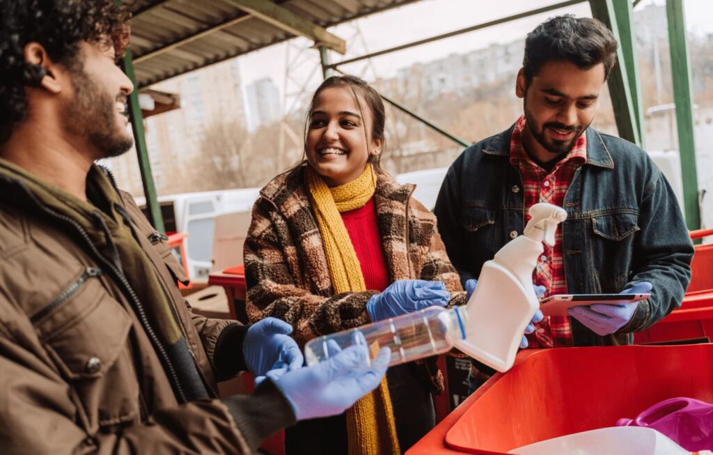 One woman and two men sort supplies into large red bins.