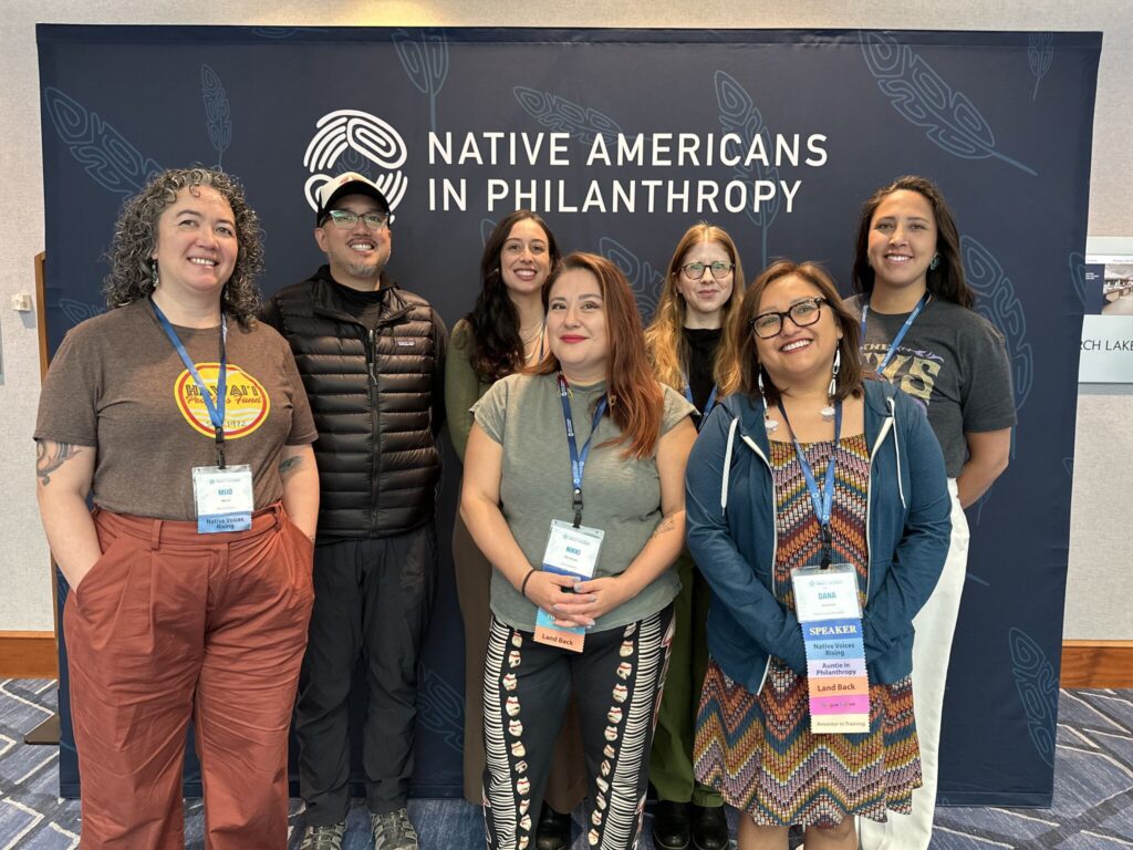 A group of six people stands in front a backdrop that says Native Americans in Philanthropy.