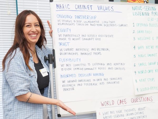 A woman stands alongside a whiteboard featuring Magic Cabinet values and a meeting agenda.